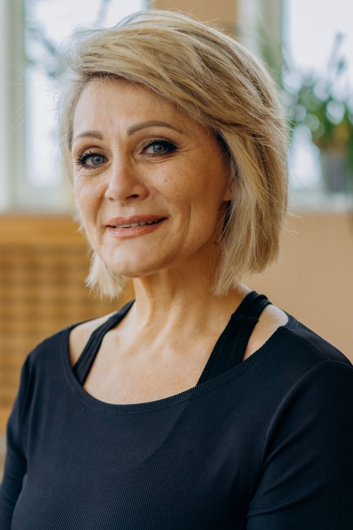 Charming senior woman with blonde hair smiling warmly, indoors. Soft lighting enhances her natural elegance.